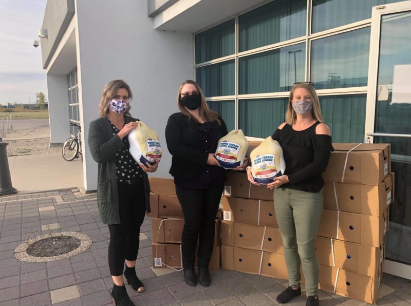 three people holding uncooked donated turkeys