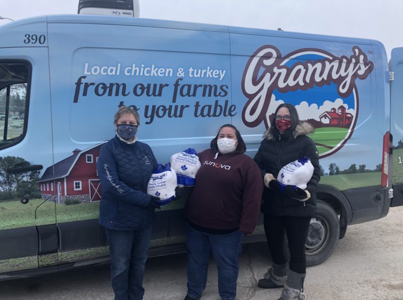 3 people standing in front of a van holding donated turkeys